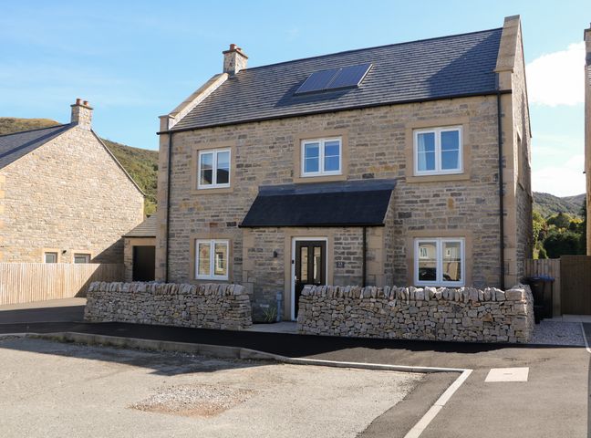 A stone house with a tiled roof solar panels and a low stone wall in front at Knoll View in Bradwell
