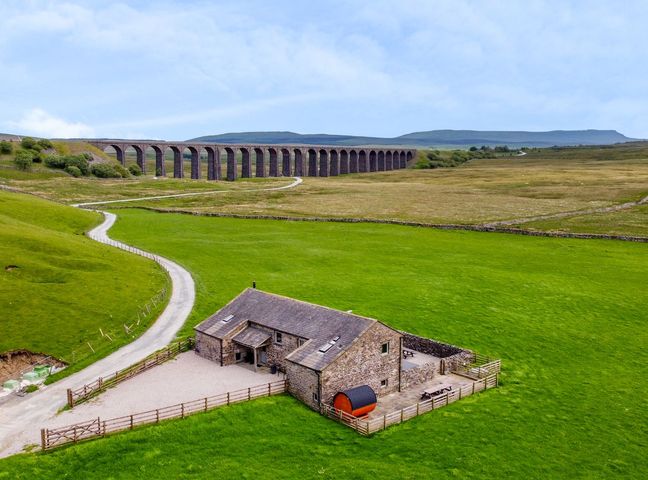 A stone house with fenced yard in green fields near a viaduct at Three Peaks Barn in Chapel-Le-Dale