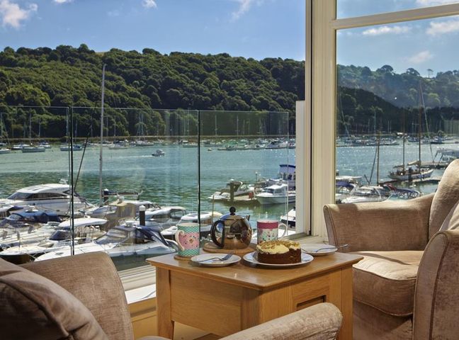 Two chairs and a wooden table with tea and cake by a large window overlooking boats on a marina at 22 Dart Marina in Dartmouth