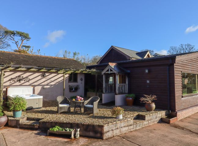 An outdoor patio area with two wicker chairs and a small table near a hot tub and plants at Sherway Dairy in Clyst Hydon near Bradninch