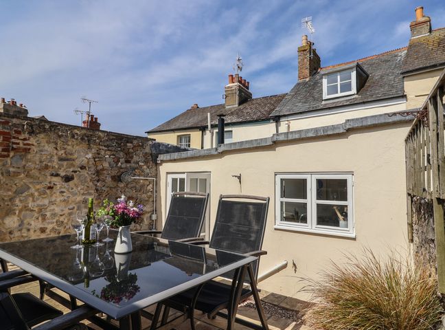 An outdoor patio area with a glass table and black chairs with flowers and wine glasses at 47 Church Street in Lyme Regis