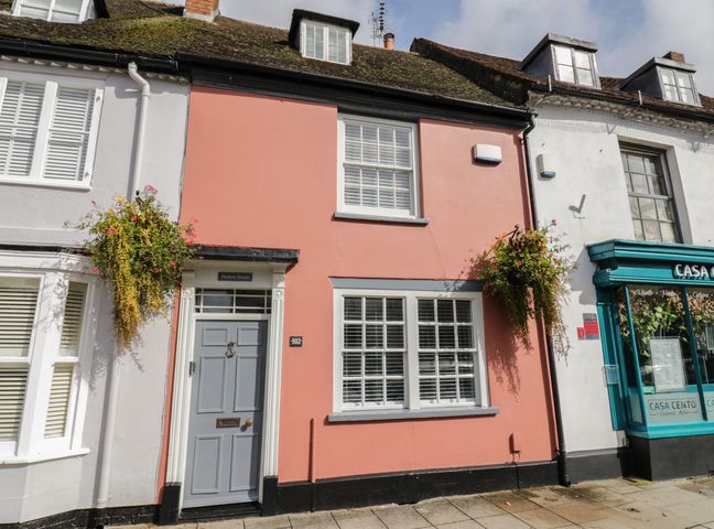 The front view of a pink painted house with a gray door and white window shutters with hanging flower baskets at Hudson House in Stony Stratford