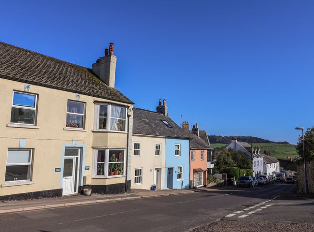 A street with pastel colored houses and parked cars under a clear sky at Charleston Cottage in Charmouth
