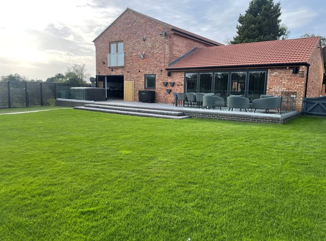 A brick house with a tiled roof and a patio with outdoor seating overlooking a lawn at 85A Braybrooke Road in Desborough