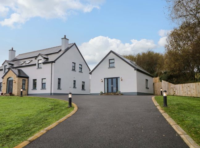 A driveway leading to two white houses with black trim and a green lawn at Coastal Hideaway in Dromore near Mountcharles County Donegal