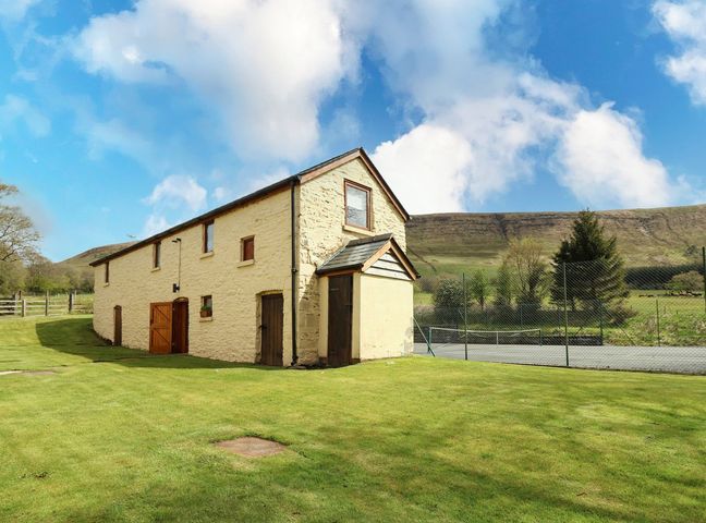 A stone building with multiple doors and windows on a grassy area with hills in the background at The Shepherd's Bothy on Blaenbrynich Farm Libanus near Sennybridge