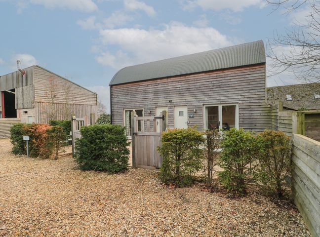 A wooden barn style building with small hedges and a gate in front of it at Dutch 2 in Lechlade-On-Thames