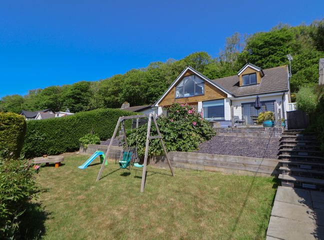 A backyard with a swing set slide and garden toys in front of a house with a patio and stairs at Buzzards View in Dyserth