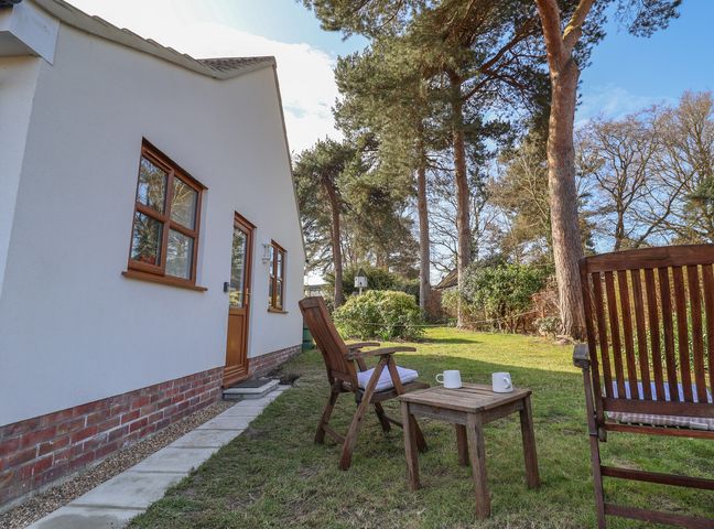 A garden with wooden chairs and a small table with two mugs outside a white house at West End in Martlesham Village