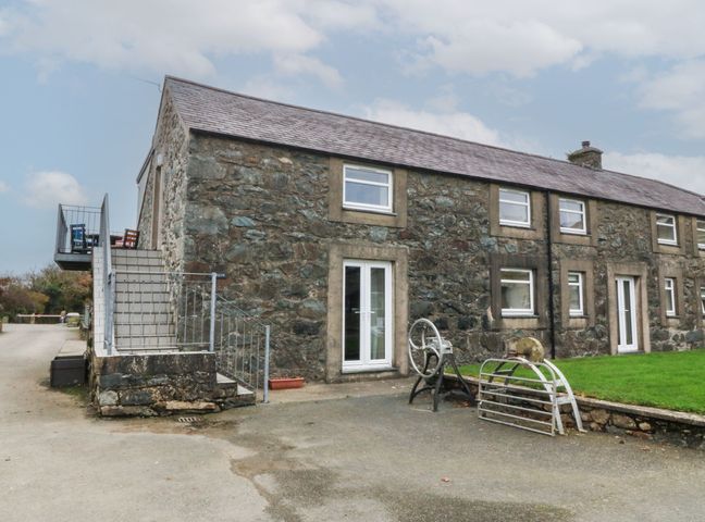 A stone building with multiple windows and doors a metal staircase on the left and a grassy area on the right at Cwellyn in Pwllheli