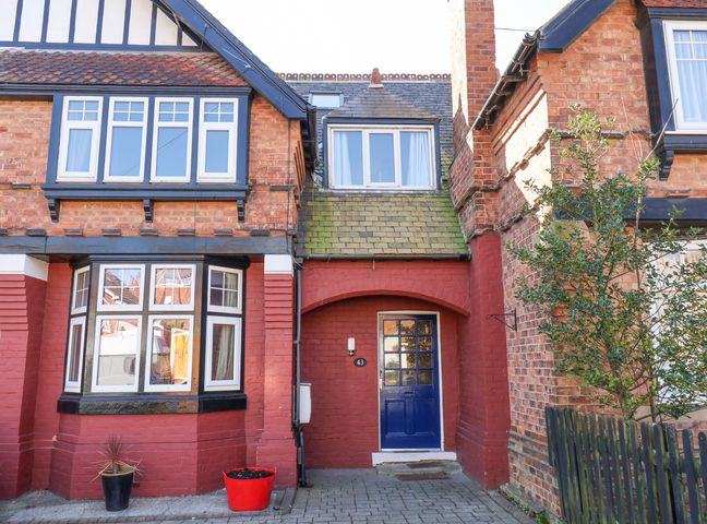 The front view of a red brick house with a blue door two flower pots and a tree near a black fence at 43 Springvale Whitby
