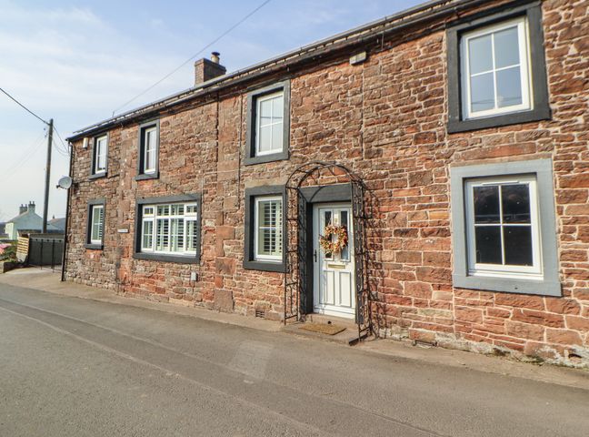 An exterior view of a stone house with a door and windows at Daisy Cottage near Wigton