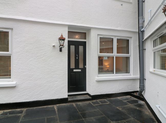 A black front door with windows on either side and a wall-mounted lamp in a white exterior at Denning Cottage in Dartmouth