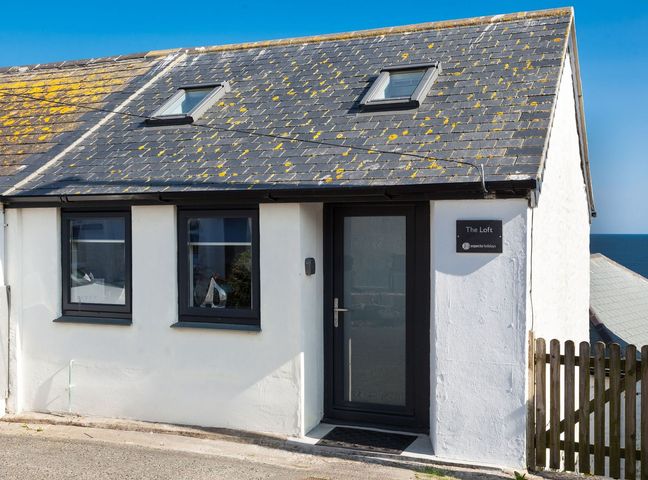 The front of a white house with two windows two skylights a black framed door and a wooden gate at The Loft in Porthleven