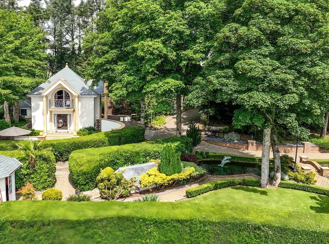 A garden with trimmed hedges a small pond a white house and trees at Hunters Moon in Charlestown