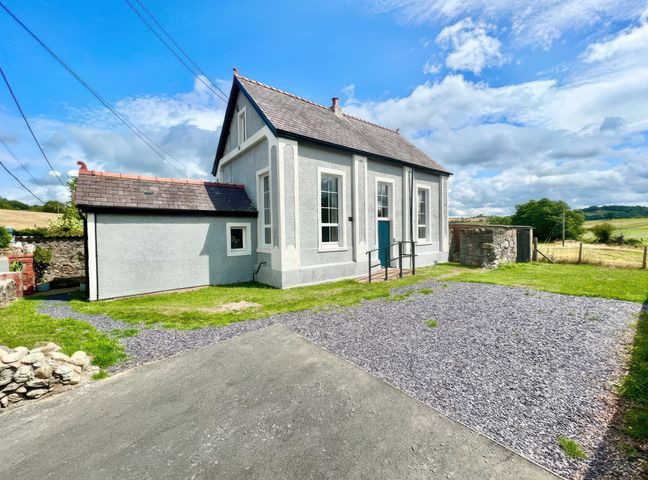An exterior view of a detached house with multiple windows and a blue door surrounded by grass and gravel at The Vestry Conwy near Conwy