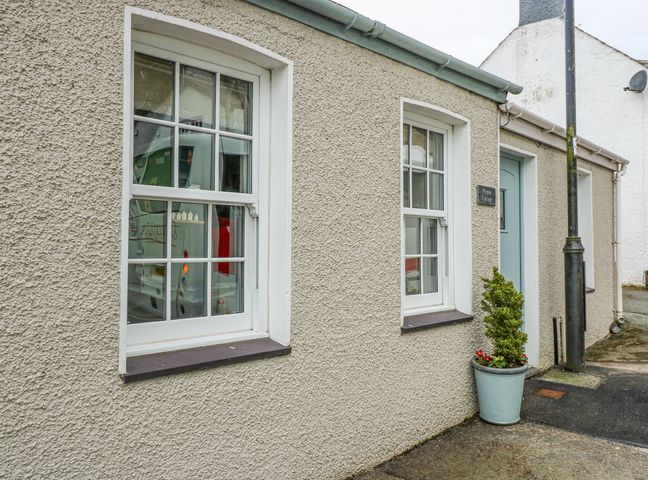 A stone building facade with two white framed windows a blue door a potted plant and a street lamp at Pippin Cottage in Beaumaris