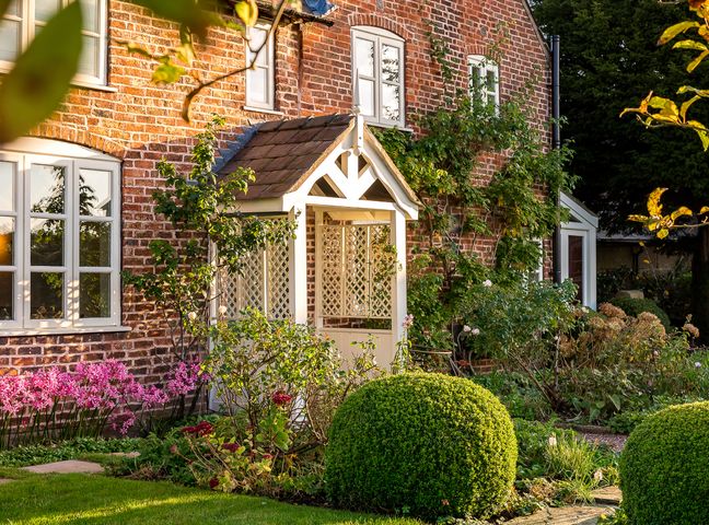 Brick house with white windows porch and garden with bushes and flowers at Wheelwrights Cottage in Tarporley