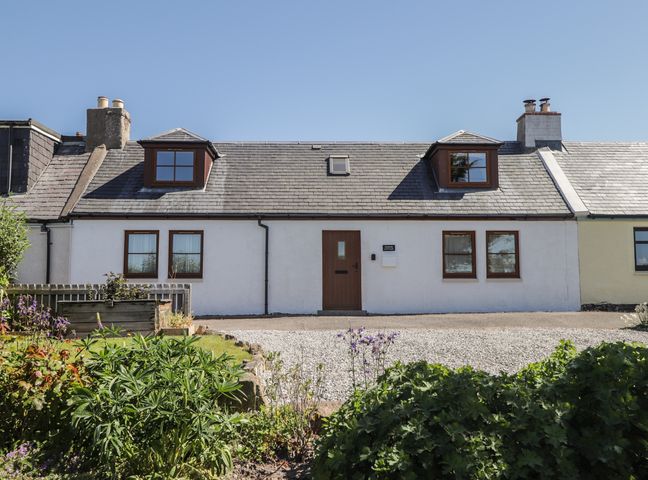 A white cottage with two dormer windows a brown door and garden in front at Fishers Cottage in Ardersier