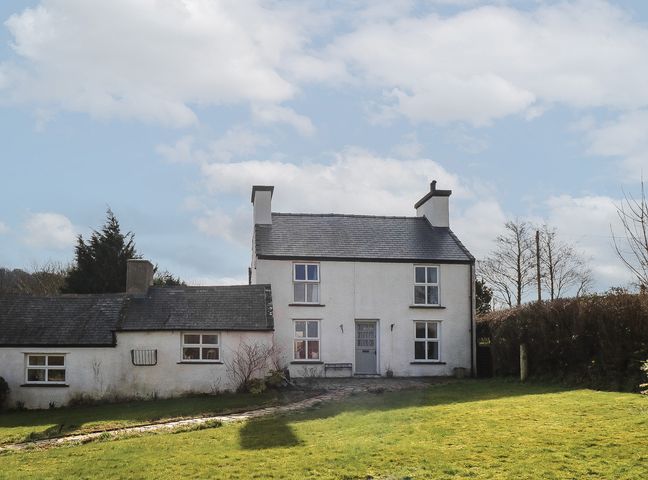 A two-story white house with chimneys and multiple windows surrounded by a grassy yard at Melin Rhos Farm in Rhoslligwy near Moelfre