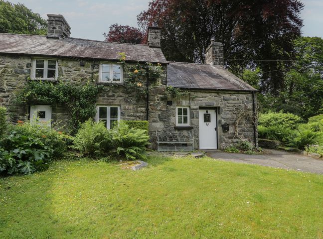 A cottage with a door and windows surrounded by grass and plants at Glandwr Cottage Llanbedr