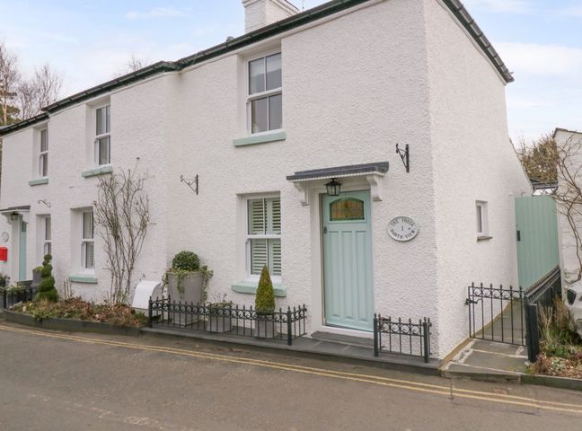A white exterior house with a light blue door and small garden area at The Fossa in Cartmel