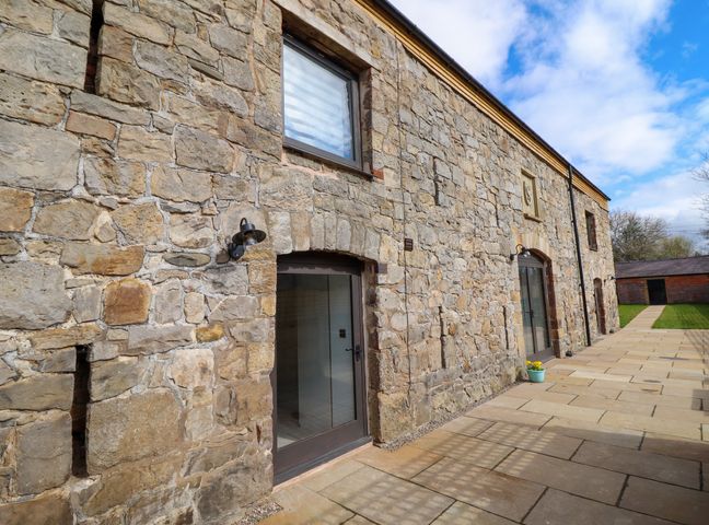 A stone building exterior with doors windows and lights on a paved walkway at Threshers Barn in Weston Rhyn