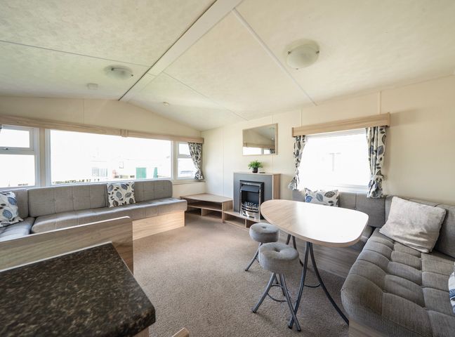A living area with built-in sofas around a dining table and an electric fireplace at Duckling Den - Billing Aquadrome in Billing Aquadrome Holiday Park
