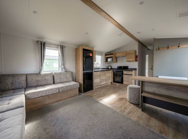 An open living space with a sofa, kitchen area, black refrigerator, oven, and dining bench at Kingfisher Caravan - Billing Aquadrome Holiday Park