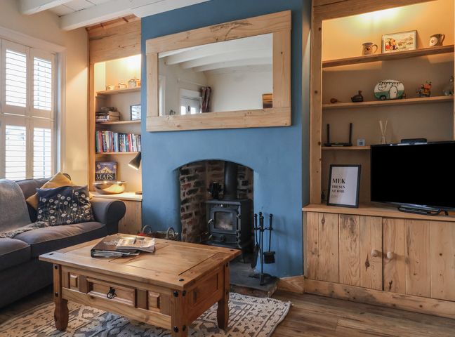 A living room with a wood stove fireplace a wooden coffee table and a sofa at Lychgate View Cottage in Aldbrough