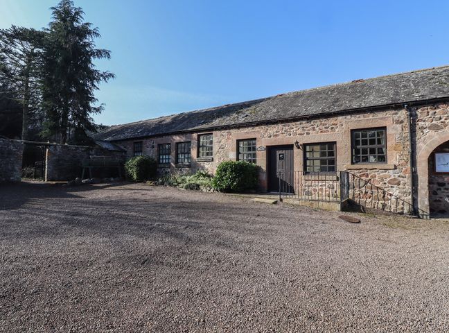 A stone building with several windows and a door with a gravel courtyard at Periwinkle in Akeld near Wooler