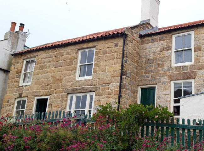 Stone cottage with green doors and windows behind a green picket fence with flowers at Pinjarra in Staithes