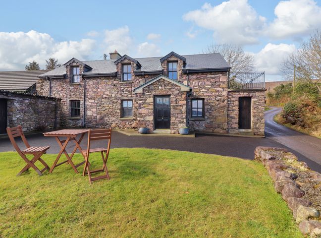 A stone house with black doors and windows and a wooden table with two chairs on grass at Johnson's Cottage in Brandon near Cloghane