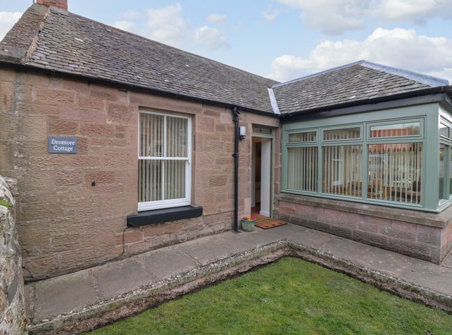 The exterior of a single-story stone cottage with a tiled roof and a small garden at Dromore Cottage in Norham