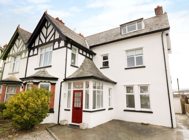 A semi detached house with white walls black trim and a red front door at 51 Trinity Avenue in Llandudno