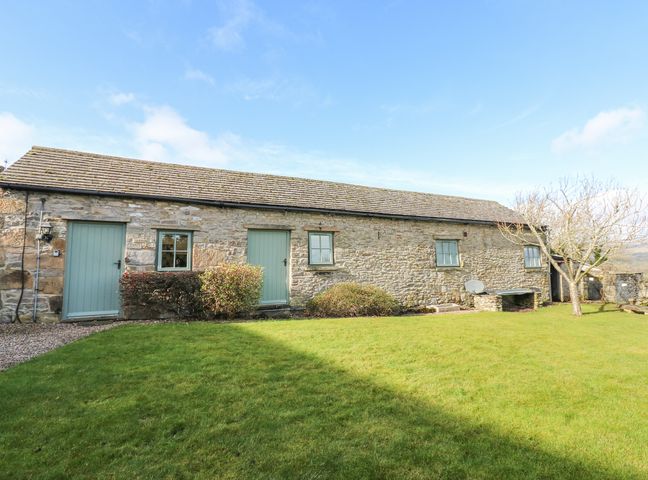 Stone building with green doors and windows with grass and bushes in front at Prospect Barn in West Witton