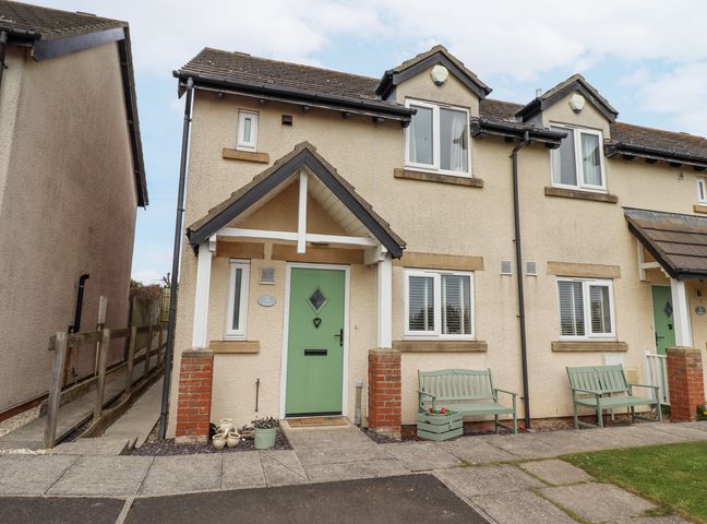 A semi detached house with green front doors benches and flower pots outside at Tee View in Seahouses
