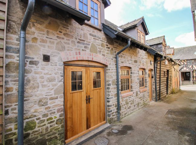 A stone building with wooden doors and windows on a paved street at The Hideaway in Bishop's Castle