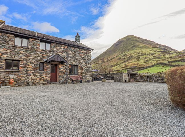 A stone house with a wooden door and bench on a gravel yard with a mountain in the background at Low Wood View in Hartsop