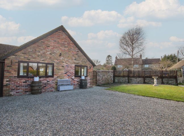 A brick building with two windows a bench and two barrels on a gravel area next to a lawn with a birdbath at Blockley Lodge in Wall-Under-Heywood