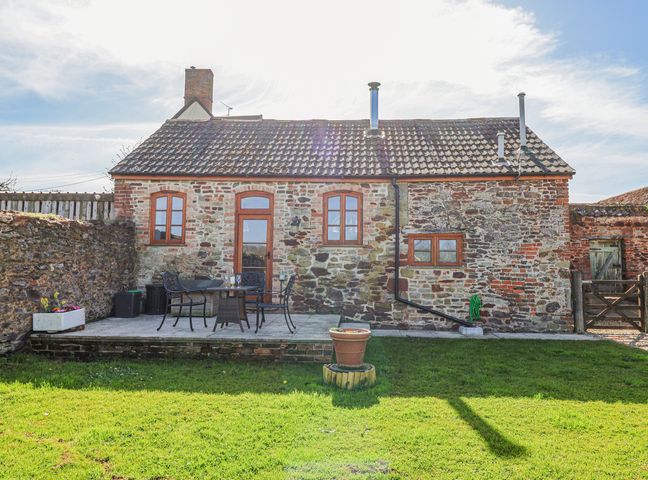 A stone cottage with a tiled roof and wooden door with windows and patio furniture on a paved area at The Yarde Annexe in Pen Elm near Taunton