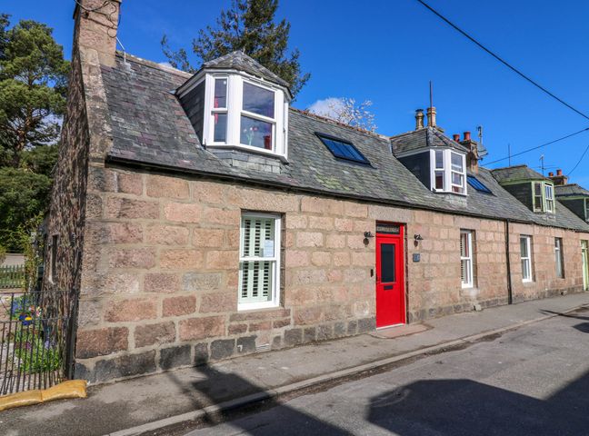 A street view of a stone house with a red door and white framed windows at Evansford in Ballater