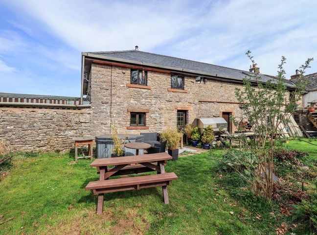 A stone house with small windows and wooden doors a wooden picnic table on grass and plants at Howdy Barn in Great Strickland