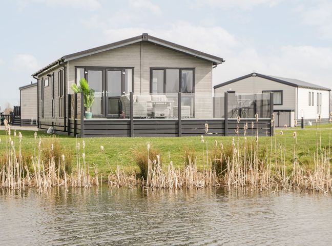 A holiday lodge with a deck and outdoor furniture by a pond at Summerdown in Brean