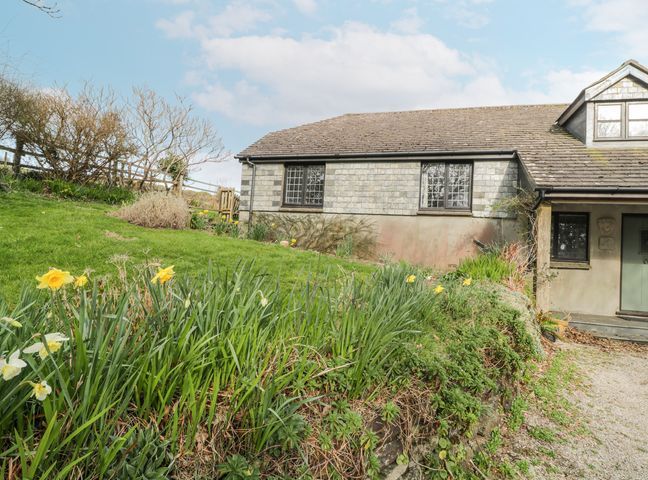 Exterior view of a stone house with a tiled roof and green door with flower garden and grass in front at Wringford Farm Annexe in Rame near Kingsand