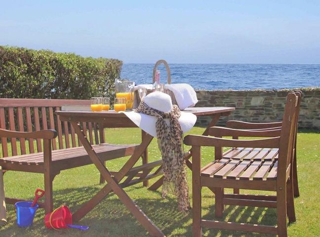 A wooden outdoor table and benches on grass with orange juice glasses and a sunhat near the sea at Watchtower Downderry near Looe
