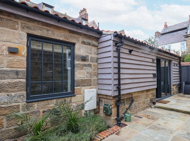 Exterior view of a stone and wood sided building with windows and a paved patio at The Old Jet Workshop in Whitby