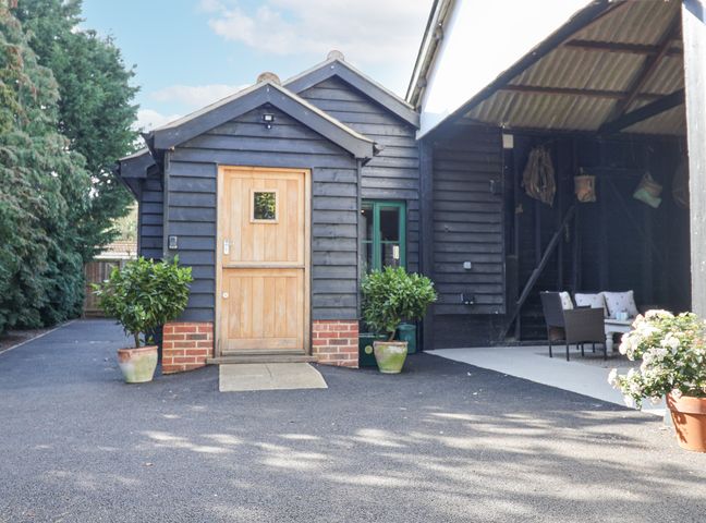 A black wooden building with a wooden door two potted plants and an outdoor seating area with chairs and a table at Bradleys Barn in Boxted near Great Horkesley