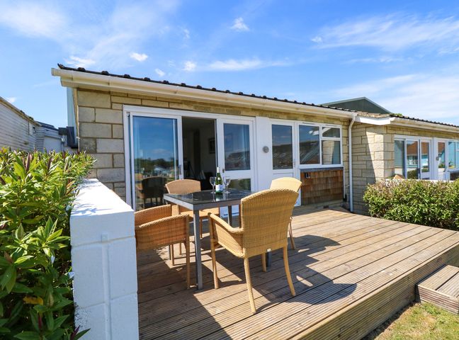 An outdoor wooden deck with a table and four wicker chairs outside a stone house at Cape 14 in Yarmouth