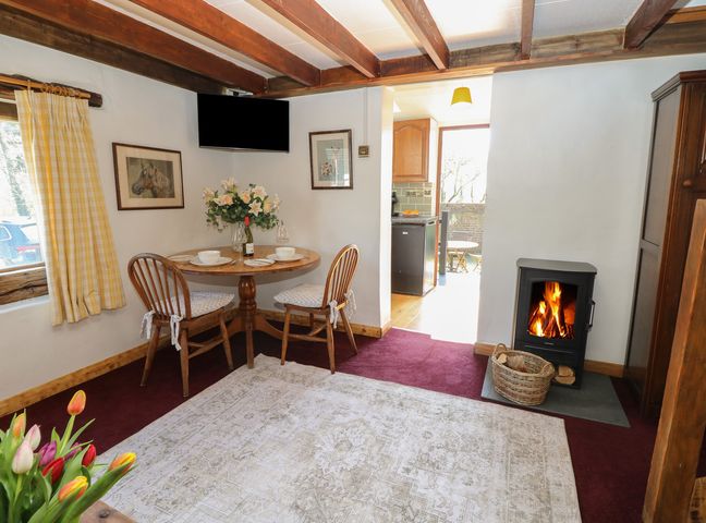 A dining area with a round table and two wooden chairs beside a wood burning stove in a room with exposed ceiling beams at The Granary Hill Farm near Freshwater